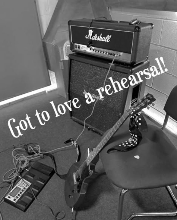 Black and white photo of a Marshall amp, a guitar resting on a chair and an effects board in a rehearsal room